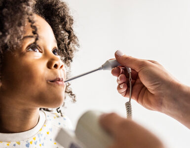 A young girl at a doctor's office, having her temperature taken while looking at the physician's face.