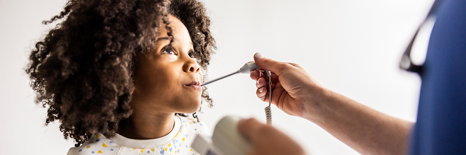 A young girl at a doctor's office, having her temperature taken while looking at the physician's face.