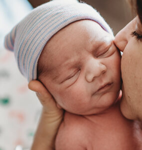 A mother holding her newborn baby, kidding his cheek.