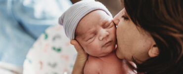 A mother holding her newborn baby, kidding his cheek.