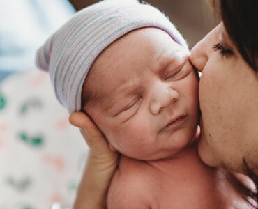 A mother holding her newborn baby, kidding his cheek.