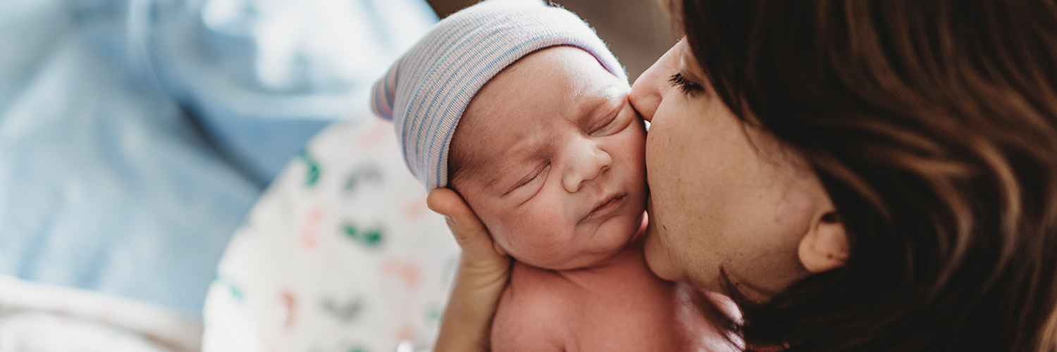 A mother holding her newborn baby, kidding his cheek.