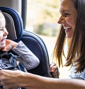 A mother buckling her toddler daughter into her car seat.