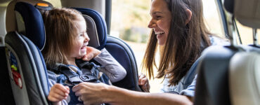 A mother buckling her toddler daughter into her car seat.