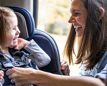 A mother buckling her toddler daughter into her car seat.