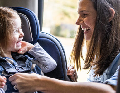 A mother buckling her toddler daughter into her car seat.