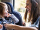 A mother buckling her toddler daughter into her car seat.