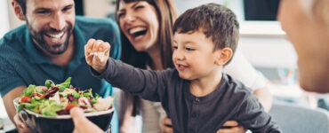 A family working together to prepare a salad, with a little boy helping and smiling.