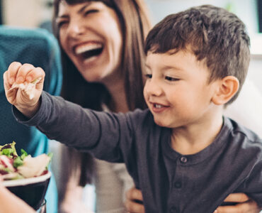 A family working together to prepare a salad, with a little boy helping and smiling.