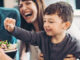 A family working together to prepare a salad, with a little boy helping and smiling.