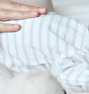 An infant laying down and crying, with mom's hand on his belly.