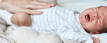 An infant laying down and crying, with mom's hand on his belly.
