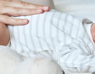 An infant laying down and crying, with mom's hand on his belly.