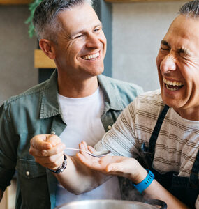 Two middle-aged men cooking dinner together in a kitchen while laughing.