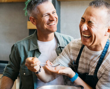 Two middle-aged men cooking dinner together in a kitchen while laughing.