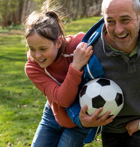 A grandfather playing soccer outdoors with his grandchildren.