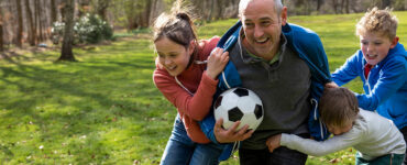 A grandfather playing soccer outdoors with his grandchildren.