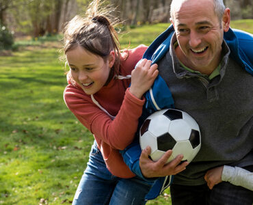 A grandfather playing soccer outdoors with his grandchildren.