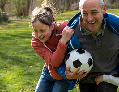 A grandfather playing soccer outdoors with his grandchildren.