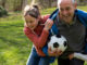 A grandfather playing soccer outdoors with his grandchildren.