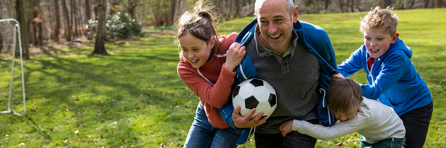 A grandfather playing soccer outdoors with his grandchildren.