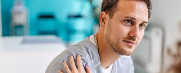 A young man sitting in a doctor's office, being consoled by the nurse.