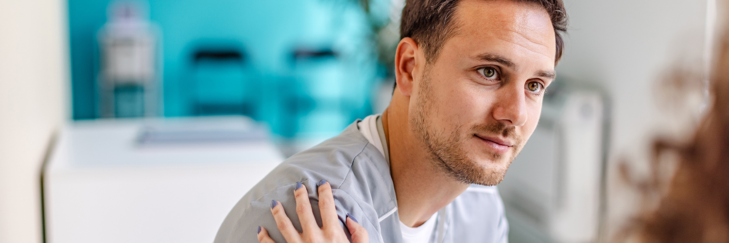 A young man sitting in a doctor's office, being consoled by the nurse.