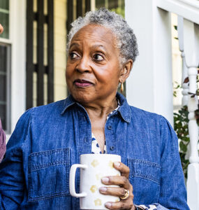 An older black woman sitting next to her daughter on her front stoop, drinking a cup of coffee.