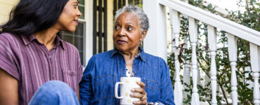 An older black woman sitting next to her daughter on her front stoop, drinking a cup of coffee.
