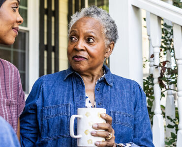 An older black woman sitting next to her daughter on her front stoop, drinking a cup of coffee.