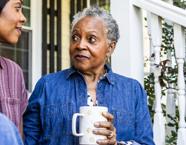 An older black woman sitting next to her daughter on her front stoop, drinking a cup of coffee.