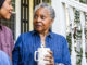 An older black woman sitting next to her daughter on her front stoop, drinking a cup of coffee.