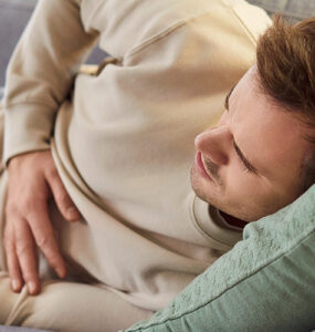 A young man laying on the couch, holding his stomach in pain.