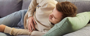 A young man laying on the couch, holding his stomach in pain.