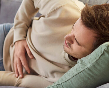A young man laying on the couch, holding his stomach in pain.