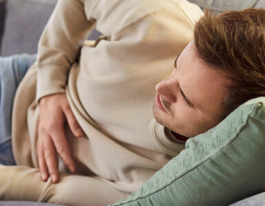 A young man laying on the couch, holding his stomach in pain.