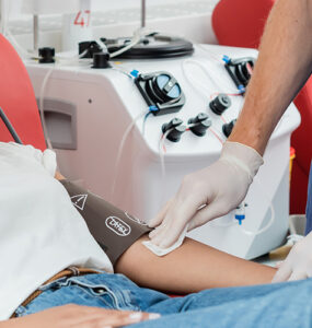 A young woman laying in a red chair, donating blood with the help of a nurse.