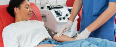 A young woman laying in a red chair, donating blood with the help of a nurse.