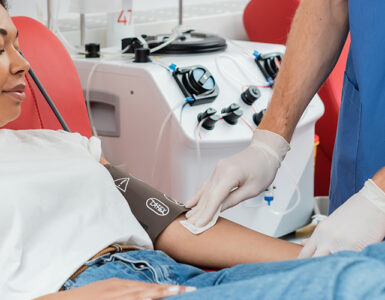 A young woman laying in a red chair, donating blood with the help of a nurse.