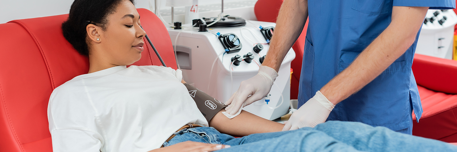 A young woman laying in a red chair, donating blood with the help of a nurse.