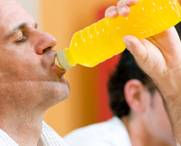 A middle-aged man drinking an energy drink from a bottle while standing in the gym.