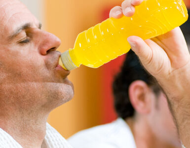 A middle-aged man drinking an energy drink from a bottle while standing in the gym.