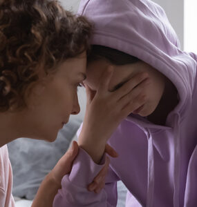 A mother consoling her grieving child who has her hand covering her eyes.