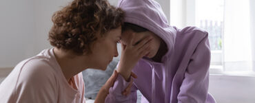 A mother consoling her grieving child who has her hand covering her eyes.