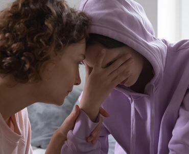 A mother consoling her grieving child who has her hand covering her eyes.