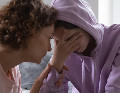 A mother consoling her grieving child who has her hand covering her eyes.