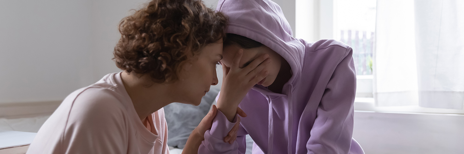 A mother consoling her grieving child who has her hand covering her eyes.