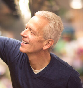 A middle-aged man reaching for fresh peppers in the grocery store.