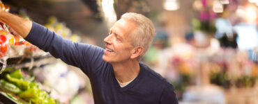 A middle-aged man reaching for fresh peppers in the grocery store.