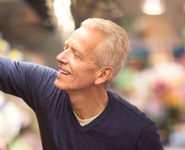 A middle-aged man reaching for fresh peppers in the grocery store.